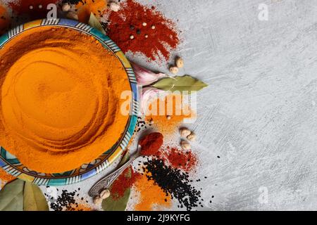 Colorful still life with turmeric powder on blue handmade plate. Close up photo of different spices on light grey background. Stock Photo