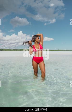 young tan asian female with long dark hair and a red swimsuit standing in turquoise blue ocean on Leebong private island with white sand beach Stock Photo