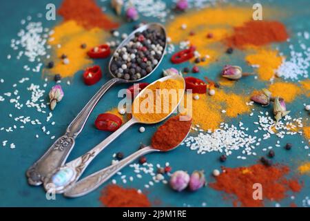 Still life with silver spoons, turmeric , paprika powder, bay leaf and pepper. Vibrant colors of Indian spices. Aromatic spices and herbs on a table. Stock Photo