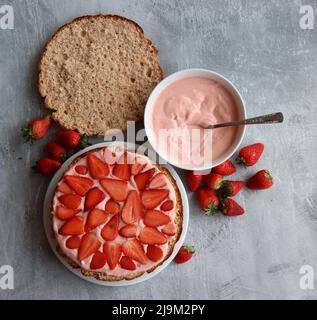 Strawberry cake in process. Close up photo of strawberry tart ingredients on a table. Fresh berries, dairy cream, cake layers top view. Stock Photo