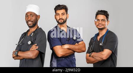 attractive medical team standing together over light gray background. African American nurse and two Indian doctors Stock Photo
