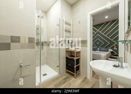 Bathroom with shower cabin with glass door, wooden furniture and white porcelain sink Stock Photo