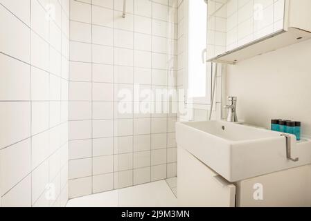 Small toilet with white porcelain sink, square white tiled shower and mirror on white wooden cabinet Stock Photo