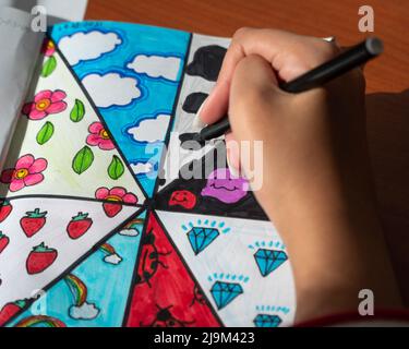 Hand of a talented young girl creatively drawing artwork on a note book placed on a wooden desk. Stock Photo