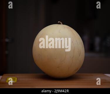 Fresh ripe Honeydew Melon placed on a wooden cutting board with a dark background. Stock Photo