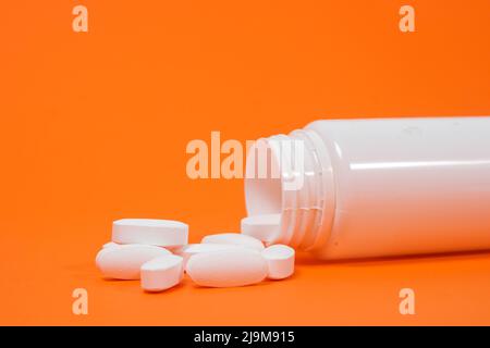 Large white pills spill out of a white jar on an orange background Stock Photo
