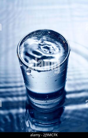 Blue monochrome image of water splashing in a glass. Stock Photo
