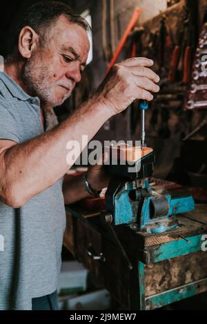 Side view of attentive mature male mechanic using screwdriver and repairing old tractor headlight while working in shabby garage Stock Photo