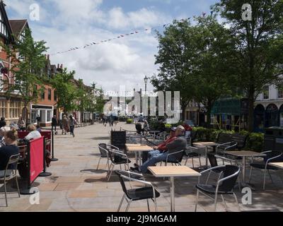 People sitting in sunshine in pedestrianised square Henley-on-Thames Oxfordshire England UK view down main street to St Mary's Church Stock Photo