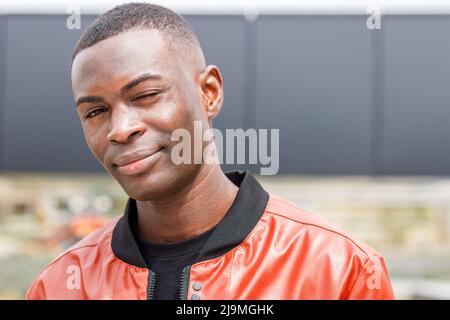 Self assured happy young African American male millennial in black t shirt and jeans standing on street looking at camera on sunny day Stock Photo