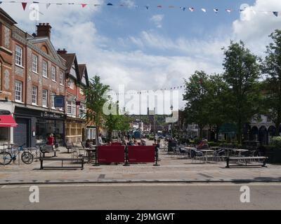 People sitting out in sunshine in pedestrianised square Henley-on-Thames Oxfordshire England UK view down main street to St Mary's Church on lovely Ma Stock Photo