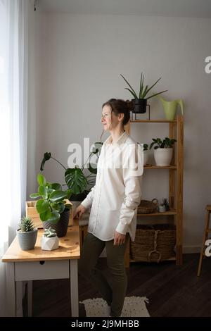 From below of young pensive African American guy in casual outfit listening to music in wireless earphones standing on staircase of modern building ag Stock Photo