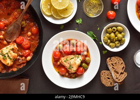 Cod stew with chickpeas, cherry tomatoes and olives over dark stone background. Top view, flat lay Stock Photo