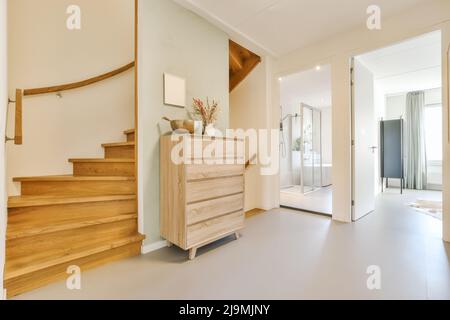 Decorative plants and vase on wooden commode near stairway in corridor of modern spacious house Stock Photo