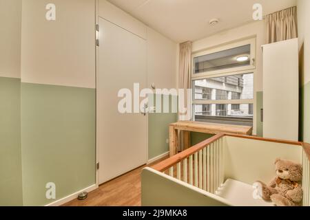 Wooden cot placed near window with curtains in light stylish spacious bedroom with green cabinets at home Stock Photo