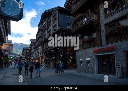 The picturesque main shopping street of Zermatt with Restaurants ,local chalet houses , hotels and shops filled with tourists captured in summer Stock Photo