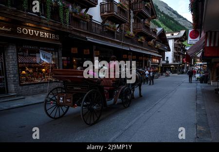 Horse coach carrying tourists on the main shopping street of Zermatt which is a eco-friendly car-free village surrounded by restaurants and shops Stock Photo