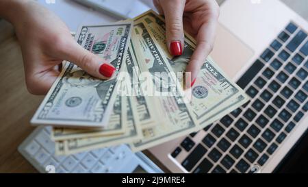 Woman hands holding dollar bills earned by working from laptop at home on Internet Stock Photo