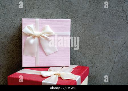Front view of two beautiful gift boxes with satin ribbon on natural concrete wall background. Pink and red gift for New Year or Christmas. Copy space Stock Photo