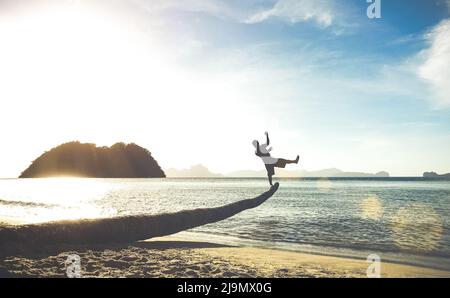 Silhouette of traveler guy on funny jump from palm - Travel wanderlust concept with man having fun at Las Cabanas beach in El Nido Palawan - Soft tilt Stock Photo