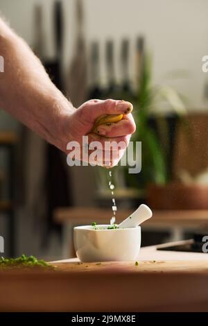 Close-up of unrecognizable mans hand squeezing fresh lemon juice into mortar with chopped parsley and grinded spices Stock Photo