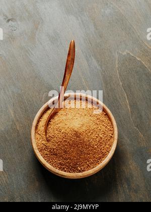 Bowl and spoon of coconut brown sugar on wooden background.Top view of full wooden bowl with raw organic coconut sugar from crystallized sap of cut flower buds coconut palm. Copy space. Vertical Stock Photo
