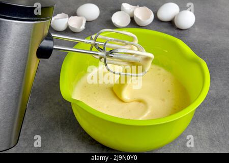 Beaten eggs with sugar and flour in a green bowl and a mixer Stock Photo