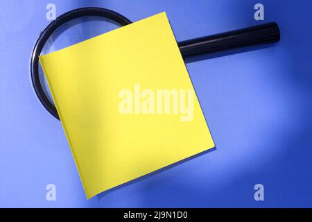 Adhesive Note With Magnifying Glass Against Blue background. Directly Above. Flat Lay. Copy Space. Business Concept. Stock Photo