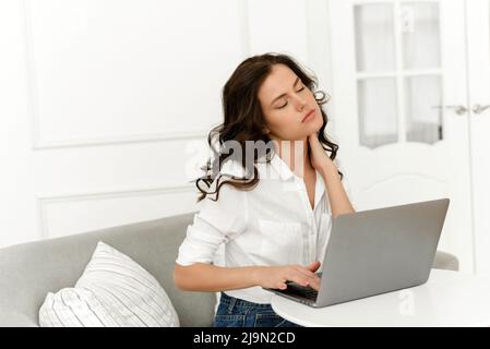 Young female freelancer working from home and experiencing neck pain. Lots of work from home. Stock Photo