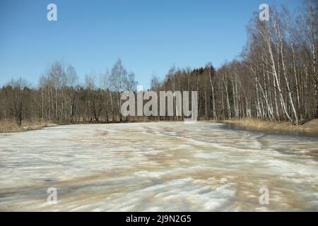 Ice is melting on lake. Spring Pond. Melted snow in forest. View of reservoir. Stock Photo