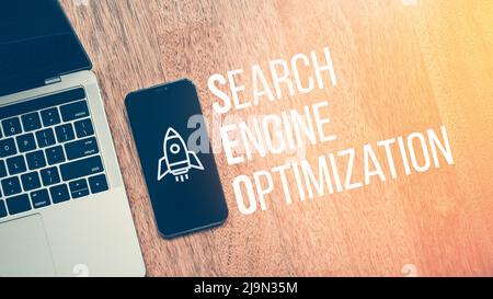 Concept Search Engine Optimization or SEO. Text with rocket icon on smartphone next to laptop Stock Photo