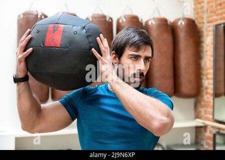 Determined athletic man with muscular body exercising with heavy medicine ball during intense workout in gym Stock Photo