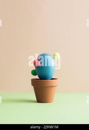Blue Easter egg arranged like a potted cactus on a green and pink background. Minimal abstract concept. Isometric layout. Square with copy space Stock Photo