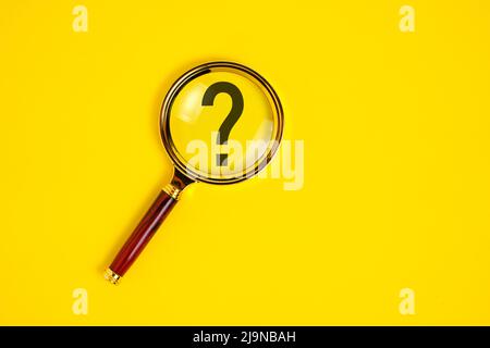 Question mark under magnifying glass, on yellow background Stock Photo
