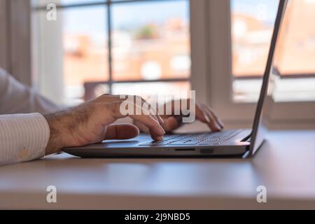 Hands of man typing a laptop keyboard at home, telecommuting. Stock Photo