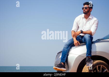 Successful young businessman sunglasses on a beach. Afro man leaning on his car parked in front of ocean on road trip enjoying peace and silence Stock Photo