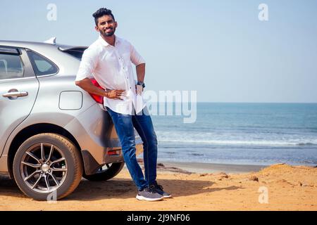travel vacation happy indian man in white shirt collar buying new car and showing the key, sitting in car on beach sea india octan Goa .a trip to the Stock Photo
