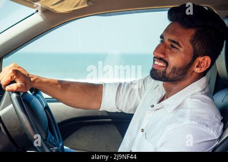 travel vacation happy indian man in white shirt collar buying new car and showing the key, sitting in car on beach sea india octan Goa .a trip to the Stock Photo