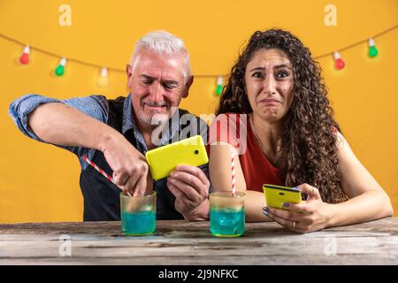 father and daughter have fun putting a smartphone into a glass full of a blue cocktail - studio shot Stock Photo