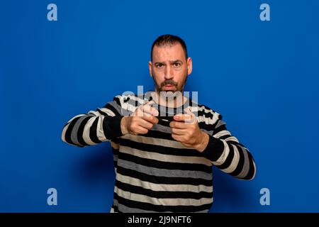 Portrait of concentrated bearded Caucasian man playing video games with a controller in his hands, isolated on blue studio background Stock Photo