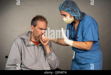 Medical care image of a man in a wheel chair coughing being comforted by a worried nurse in gloves and mask. Stock Photo