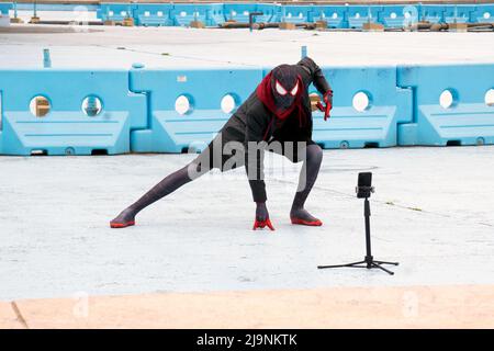 With the aid of a tripod, Spiderman takes some selfies under the Unisphere in Flushing Meadows Corona Park in queens, New York City. Stock Photo