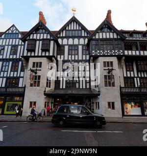 London, Greater London, England, May 11 2022: Taxi and a cyclist with an orange helmet outside Liberty designer apartment store Stock Photo