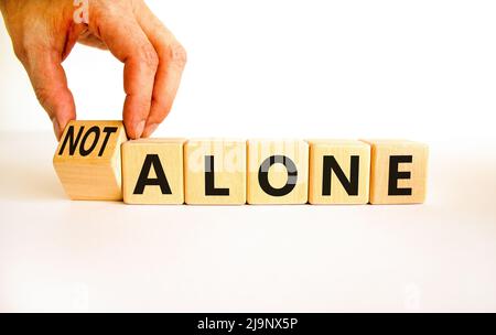 You are not alone symbol. Businessman turns wooden cubes and changes concept words alone to not alone. Beautiful white background. Business, support a Stock Photo