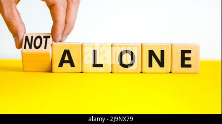 You are not alone symbol. Businessman turns wooden cubes and changes concept words alone to not alone. Beautiful white background. Business, support a Stock Photo