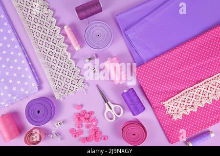 Sewing flat lay with various tools like fabric, scissors, spools and ribbons on violet background Stock Photo