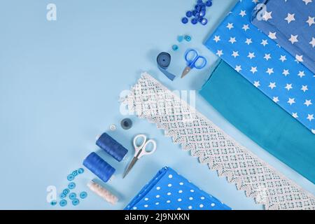 Sewing flat lay with various tools like fabric, scissors, spools and ribbons on blue background Stock Photo