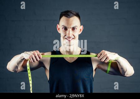 A young man measures his hand with a measuring tape in the gym on a dark background Stock Photo