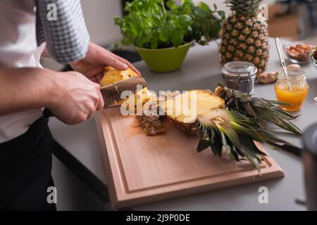 A man standing behind bar counter cutting a pineapple on chopping board. Stock Photo