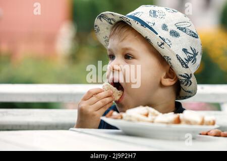 Close-up portrait of cute little child eating bread in green garden, outdoors. Summer lifestyle. Homegrown organic food. A healthy children nutrition. Stock Photo